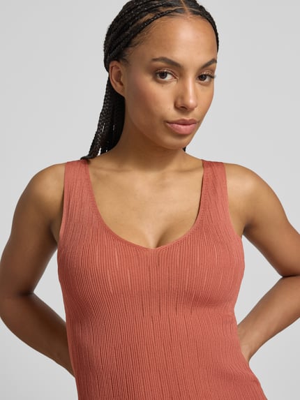 Vrouwenmodel draagt Stricktop aus Viskose-Mix mit V-Ausschnitt van Marc Cain, viscosemix, nauwsluitende fit, V-hals, labeldetail, roestrood, ribtextuur, close-up bovenlichaam
