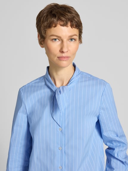 Kobiece model prezentuje Slim Fit Schluppenbluse mit Knopfleiste od Stefanel, bawełniany miks z dodatkiem stretchu, krój slim fit, stójka, zapięcie na guziki, długość tyłu w rozmiarze S: 60 cm, długość rękawa w rozmiarze S: 62 cm, jasnoniebieska, pionowe białe paski, tekstura gładka, zbliżenie na górną część ciała.