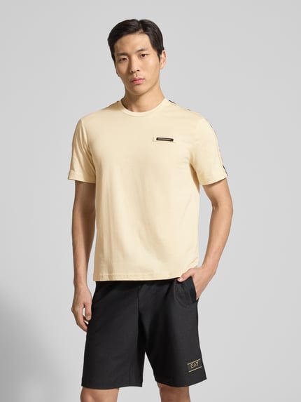 Männermodel trägt Regular Fit T-Shirt mit Logo-Patch von EA7 Emporio Armani in Beige, reine Baumwolle, Rundhalsausschnitt, Ganzkörperansicht von vorne.