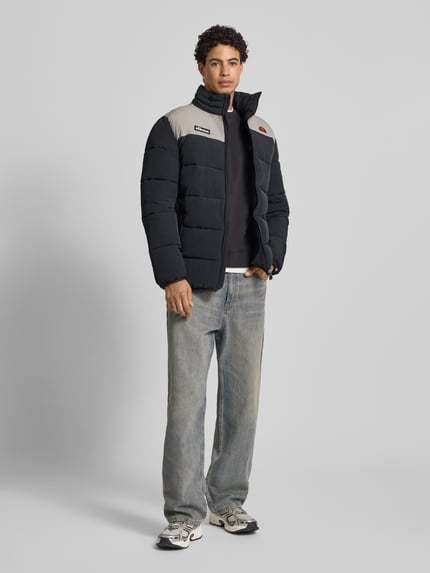 Mannenmodel draagt gewatteerd jack met ritssluiting model 'NEBULA' van Ellesse, regular fit, opstaande kraag, labeldetails, steekzakken, ruglengte maat M 77 cm, schouderbreedte 49 cm, borstwijdte 57 cm, mouwlengte 70 cm, kleuren zwart en grijs, doorgestikte naden, ganzekörperaanzicht van voren.