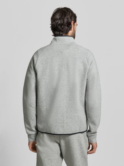 Męski model nosi Regular Fit Pullover mit Logo-Print Modell 'Unstoppable' von Under Armour, elastyczna mieszanka materiałów, kołnierz zapinany, wpuszczane kieszenie, kolor jasnoszary, długość tyłu w rozmiarze M: 66 cm, długość rękawów w rozmiarze M: 73 cm, widok całej sylwetki z tyłu.