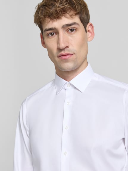 Männermodel trägt Super Slim Fit Businesshemd mit Kentkragen von OLYMP in Weiß, Webware, einreihige Knopfleiste, Nahaufnahme Oberkörper.
