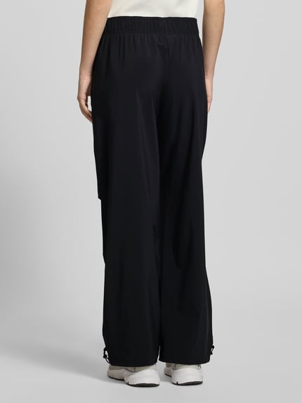 Frauenmodel trägt Wide Fit Stoffhose mit Logo-Print von adidas Sportswear in Schwarz, elastischer Bund, glatte Textur, Ganzkörperansicht Rückansicht.