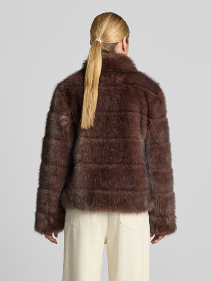 Frauenmodel trägt Jacke aus Kunstfell mit Steppnähten von PETITE M., braune Töne, weiche Textur, Rückenlänge 67 cm, Ganzkörperansicht Rückansicht.