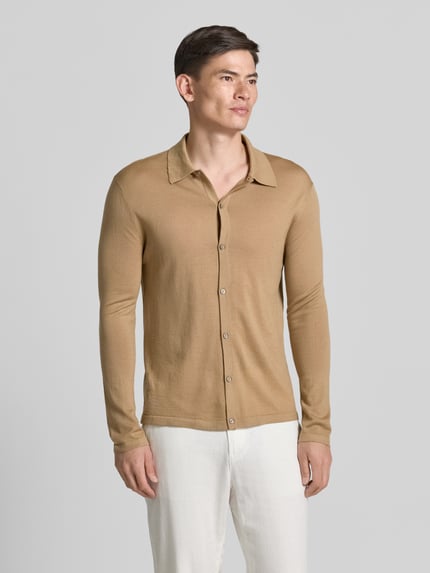Męski model nosi Regular Fit Strickjacke aus Wolle Modell 'Verklin' od Tiger Of Sweden, kolor beżowy, krój regular fit, kołnierzyk typu kent, listwa guzikowa, długość tyłu w rozmiarze M: 71 cm, długość rękawów w rozmiarze M: 65 cm, struktura gładka, widok całej sylwetki z przodu.