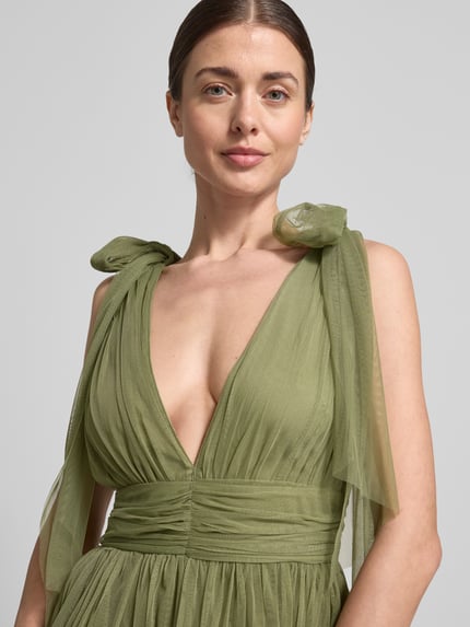 Frauenmodel trägt Knielanges Kleid mit Rüschenbesatz von LACE & BEADS in Grün aus Mesh, taillierte Passform, V-Ausschnitt, Zierschleifen, Nahaufnahme Oberkörper.