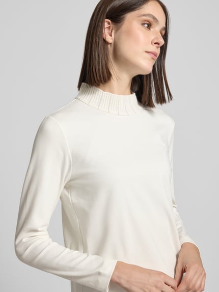 Frauenmodel trägt Langarmshirt mit Ripp Stehkragen von MARC CAIN in uni Creme, Strukturmuster, Jersey, hochgeschlossen, Nahaufnahme Oberkörper.