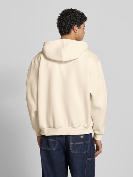 Männermodel trägt Oversized Sweatjacke mit Logo-Stitching von KARL KANI in Beige, Baumwoll-Mix, Kapuze, elastische Abschlüsse, Ganzkörperansicht Rückansicht.