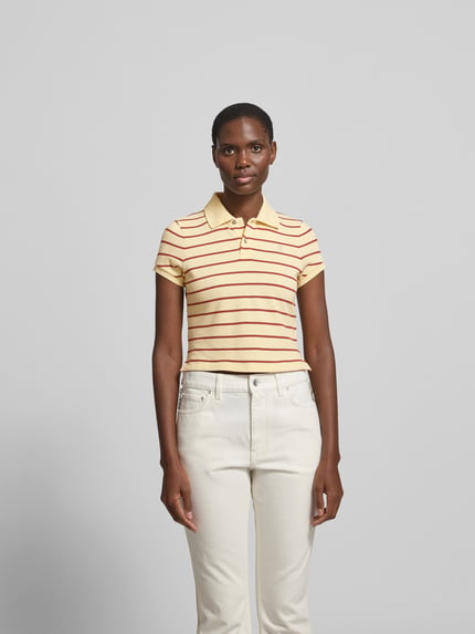 Modelka kobieta ma na sobie Cropped Poloshirt aus reiner Baumwolle od Rabanne, w żółte i czerwone paski, krótkie rękawy, kołnierzyk polo, tył wydłużony, czysta bawełna, damska koszulka, widok całej sylwetki z przodu.