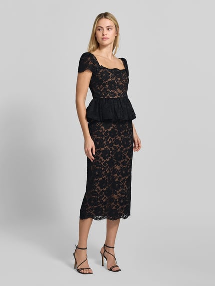 Frauenmodel trägt Abendkleid mit Spitzenpeplum von Self-Portrait in Schwarz, florales Muster, Etui Passform, breite Träger, ausgestellte Rockpartie, Midi-Länge, Spitze und blickdichter Unterrock, Ganzkörperansicht von vorne.