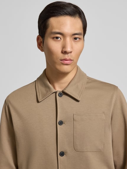 Männermodel trägt Hemdjacke mit Knopfleiste von Lindbergh in Beige, mit Brusttasche und Kentkragen, Material-Mix, Nahaufnahme Oberkörper.