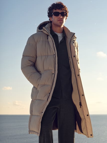 Männermodel trägt Steppmantel mit Label-Patch Modell 'Caius' von khujo in Beige, gerader Schnitt, Kapuze, Zweiwege-Reißverschluss, Ganzkörperansicht von vorne.