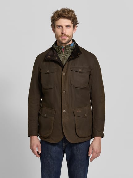 Männermodel trägt Funktionsjacke mit gewachstem Twill von Barbour in Unifarben, Stehkragen, Druckknöpfe, Langarm, Ganzkörperansicht von vorne.