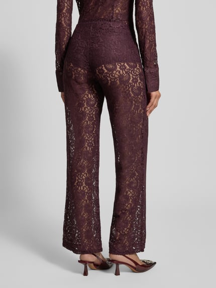 Frauenmodel trägt Stoffhose aus Spitze Modell 'GRACE' von Mango in dunklem Lila, transparenter Spitzenstoff mit Paisley-Muster, Blickdichter Unter-Pantie, Relaxed Fit, elastisches Material, Ganzkörperansicht Rückansicht.