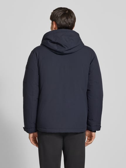 Männermodel trägt Funktionsjacke mit abnehmbarer Kapuze von BRAX in Dunkelblau, langarm, uni, Kapuze und Reißverschlusstaschen, Ganzkörperansicht Rückansicht
