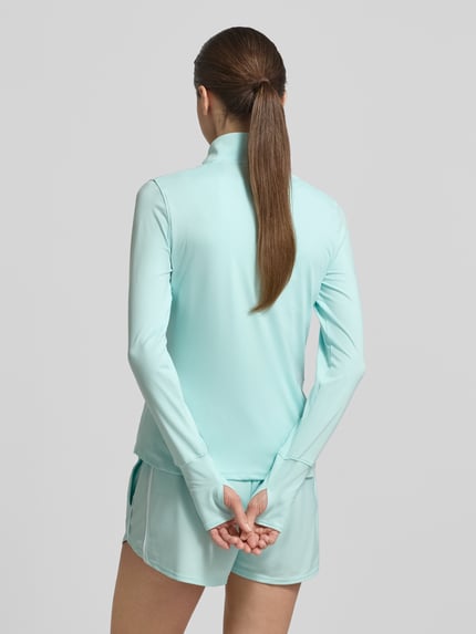 Frauenmodel trägt Longsleeve mit Stehkragen und Reißverschluss von Under Armour in hellem Türkis, Material mit Stretch, Rückenlänge 59 cm, Ganzkörperansicht Rückansicht.