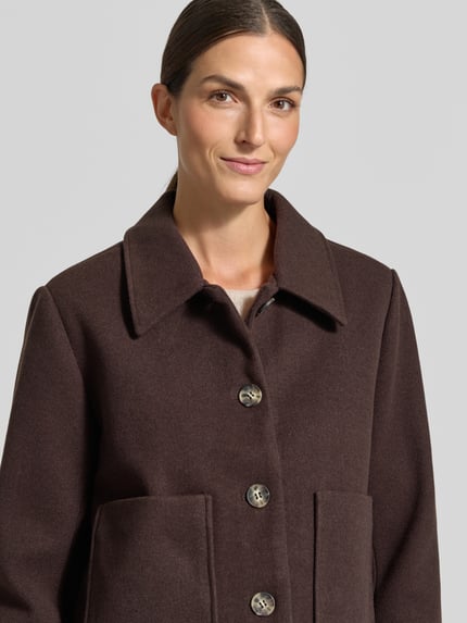 Modelka kobieca nosi Regular Fit Blouson mit aufgesetzten Taschen Modell 'JANNET' von ICHI w kolorze ciemnobrązowym, faktura gładka, guzik z przodu, kołnierz wykładany, z kieszeniami, krój regular fit, długość tyłu w rozmiarze 36: 56 cm, szerokość ramion w rozmiarze 36: 40 cm, szerokość w biuście w rozmiarze 36: 49 cm, długość rękawa w rozmiarze 36: 61 cm, zbliżenie na górną część ciała, widok z przodu.