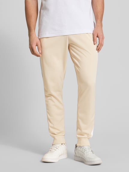 Männermodel trägt Regular Fit Sweat-Anzug mit Kontraststreifen von adidas Sportswear, unifarben, Beinabschluss gerippt, Nahaufnahme Unterkörper.