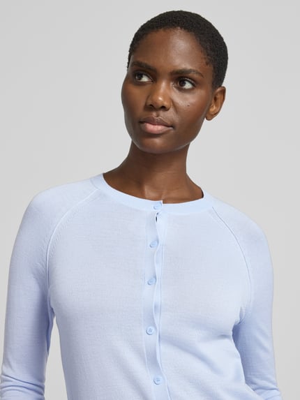 Frauenmodel trägt Strickjacke aus Wolle mit Rundhalsausschnitt von BOSS, unifarben, durchgehende Knopfleiste, Nahaufnahme Oberkörper.
