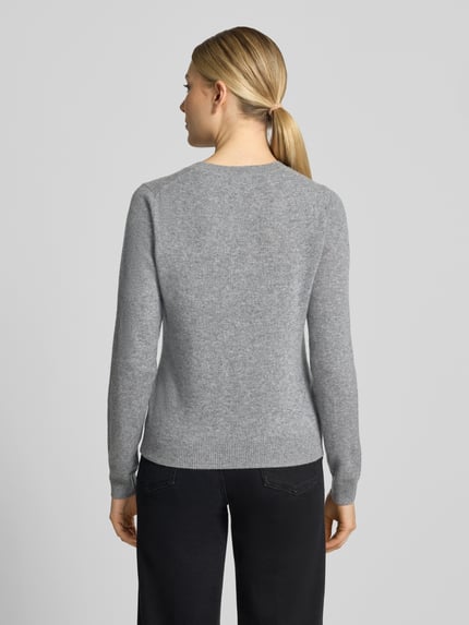 Vrouwenmodel draagt Slim Fit gebreide pullover van kasjmier Slim Fit Strickpullover aus reinem Kaschmir van Christian Berg Woman, grijze kleur, getailleerde pasvorm met elastische boordjes, Ruglengte maat S 54 cm, Mouwlengte maat S 65 cm, Ganzkörperaanzicht achteraan.