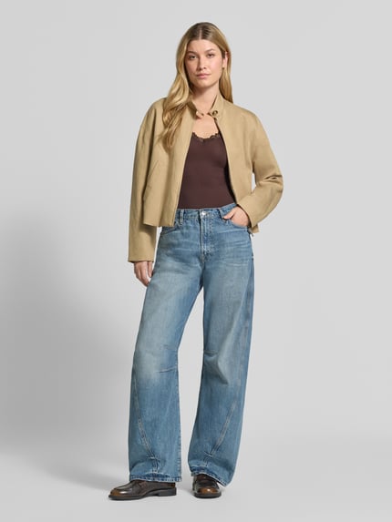 Frauenmodel trägt Slim Fit Tanktop aus Viskose-Mix Modell 'ROSA' von VERO MODA in Dunkelbraun, kombiniert mit hellblauer Jeans, Ganzkörperansicht von vorne.
