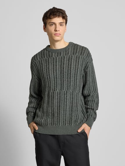 Männermodel trägt Relaxed Fit Strickpullover aus Baumwoll-Mix Modell 'FILL RLX' von Only & Sons in Zopfmuster, unifarben, Strickoptik, Ganzkörperansicht von vorne.