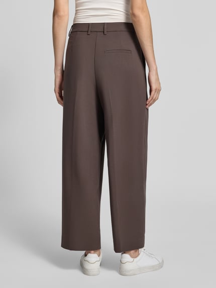 Frauenmodel trägt Anzughose mit Viskose-Anteil von COMMA in Braun, elastischer Relaxed Fit, Bundfalten, Eingriff- und Gesäßtaschen, Ganzkörperansicht Rückansicht.