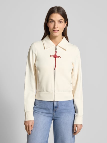 Frauenmodel trägt Slim Fit Sweatjacke aus reiner Baumwolle Modell 'EROICO' von MAX&Co., cremefarben, rote Schleife, Hemdkragen, Ganzkörperansicht von vorne