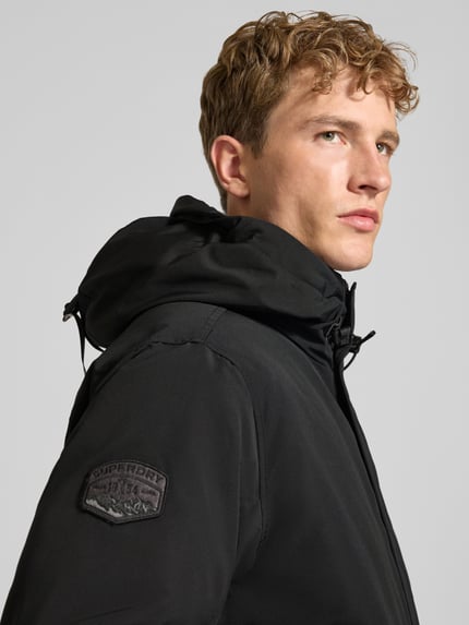 Männermodel trägt schwarze Bomberjacke mit Label-Patch Modell 'Everest' von Superdry, Regular Fit, Nahaufnahme Oberkörper.