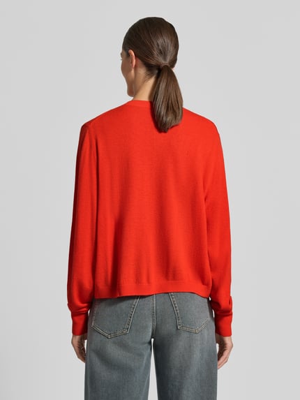 Frauenmodel trägt Relaxed Fit Strickpullover aus reiner Lanawolle mit Rippbündchen von Stefanel in leuchtendem Rot, lockere Passform, überschnittene Schultern, langärmlig, Knopfleiste und gerippte Blende, Rückansicht, Rückenlänge bei Größe S 52 cm, Ärmellänge 67 cm.