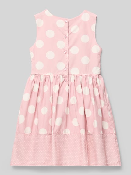 Mädchen trägt Kleid aus Baumwolle mit Rundhalsausschnitt von Happy Girls im Allover-Look, rosa mit weißen Punkten, A-Linie, Rückenansicht, Ganzkörperansicht Rückansicht. Rückenlänge bei Größe 116: 62 cm.