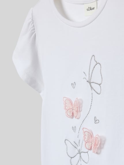 Mädchen trägt Regular Fit T-Shirt aus reiner Baumwolle von s.Oliver RED LABEL, weiß mit Schmetterling-Stitching, Kurzarm, Nahaufnahme Oberkörper.