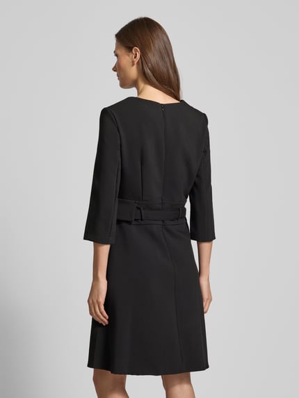 Frauenmodel trägt knielanges Cocktailkleid mit V-Ausschnitt von Rinascimento in Schwarz, taillierter Schnitt, 3/4-Ärmel, Rückansicht Ganzkörperansicht.