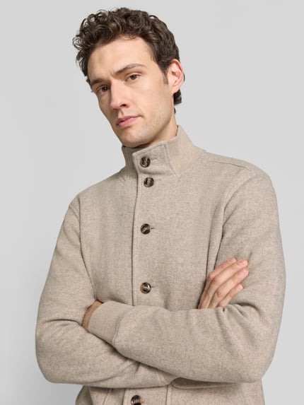 Männermodel trägt Strickjacke aus Wolle mit Stehkragen von RAGMAN in Beige, Strukturstrick, Knopfleiste, Nahaufnahme Oberkörper.