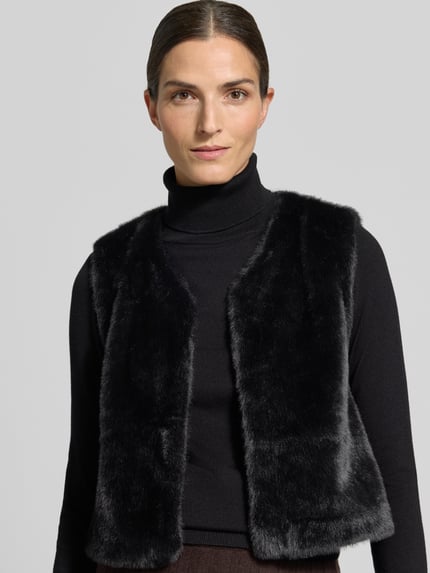 Vrouwenmodel draagt Regular Fit bodywarmer uit imitatiebont in effen design van ZABAIONE, zwart, gladde zachte textuur, Nahaufnahme bovenlichaam. Ruglengte maat S: 48 cm, schouderbreedte maat S: 36 cm, borstwijdte maat S: 48 cm.