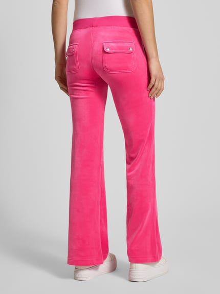 Vrouwenmodel draagt Low Rise Sweatpants met elastische band model 'LAYLA' van Juicy Couture in felroze katoenmix met stretch, flared cut, steekzakken, binnenbeenlengte maat S 39 cm, volledige lichaamsopname van achteren.