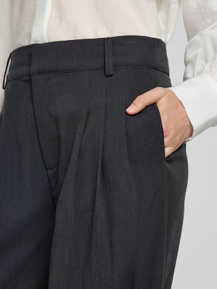 Frauenmodel trägt Barrel Fit Bundfaltenhose Modell 'Evie' von My Essential Wardrobe, dunkler Stoff, sichtbare Eingrifftasche, Nahaufnahme Oberkörper, Material-Mix mit Viskose-Anteil
