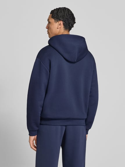 Männermodel trägt Hoodie mit Logo-Print von REVIEW aus Baumwoll-Mix in Dunkelblau, lockere Passform, Ganzkörperansicht Rückansicht.