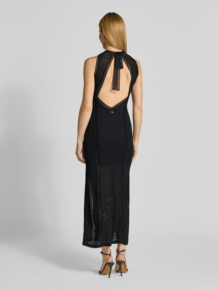 Frauenmodel trägt schwarzes Maxikleid mit Spitze und Gehschlitz Modell 'NEW LIZA' von Guess, Material-Mix, Rückansicht, Ganzkörperansicht.