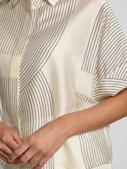 Frauenmodel trägt Boxy Fit Bluse aus Lyocell-Mix Modell 'Zulin' von Someday, cremefarben mit schwarzen Linien, Nahaufnahme Oberkörper. Damen Bluse mit Hemdblusenkragen, verdeckter Knopfleiste, Rückenlänge bei Größe 36: 60 cm, Ärmellänge 20 cm.