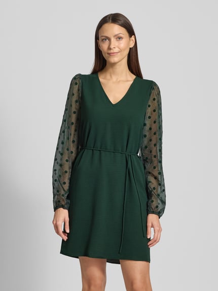 Frauenmodel trägt fließendes Cocktailkleid mit semitransparenten Ballonärmel Modell 'ALVA' von Vero Moda, Optik: Unifarben, Mini-Länge, V-Ausschnitt, Passform: Fließend, Ärmelabschluss: Elastisch, Materialverarbeitung: Crinkle, Ganzkörperansicht von vorne.