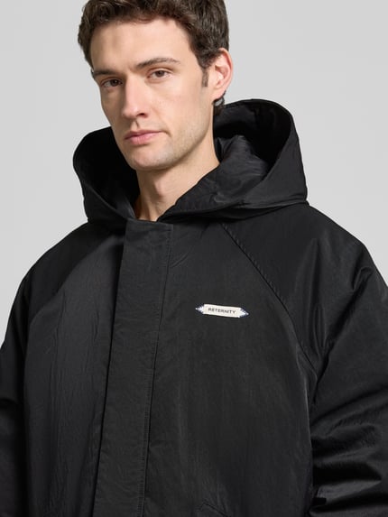 Männermodel trägt schwarze Relaxed Fit Bomberjacke mit Label-Patch Modell 'L’ATELIER' von RETERNITY, glatte Textur, Nahaufnahme Oberkörper. Rückenlänge 70 cm, Schulterbreite 37 cm, Brustweite 80 cm, Ärmellänge 79 cm.