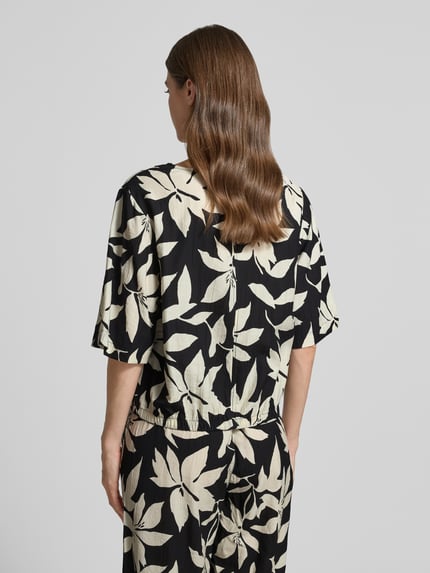 Frauenmodel trägt Relaxed Fit Blusentop aus Viskose-Mix von s.Oliver RED LABEL mit floralem Allover-Muster in Schwarz und Creme, Rückansicht.