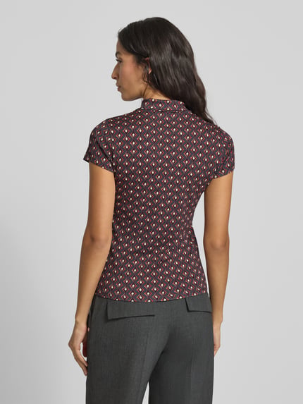 Frauenmodel trägt Slim Fit T-Shirt mit Polokragen von Marc Cain im Allover-Look aus Baumwoll-Elasthan-Mix, Rückenlänge 56 cm, Ganzkörperansicht Rückansicht.