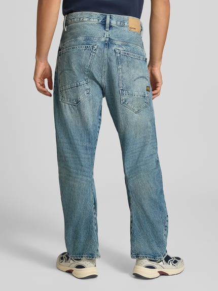 Männermodel trägt Loose Fit Jeans aus reiner Baumwolle Modell 'G-Star Arc 3D Loose' von G-Star RAW, blaue Waschung, Ganzkörperansicht Rückansicht.