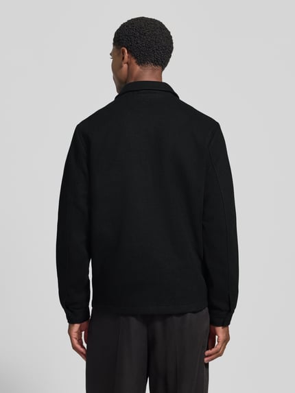 Männermodel trägt Jacke mit Brusttasche und Kentkragen Modell 'ROLFSTED' von Casual Friday in Schwarz, gerade Form, Ganzkörperansicht Rückansicht.