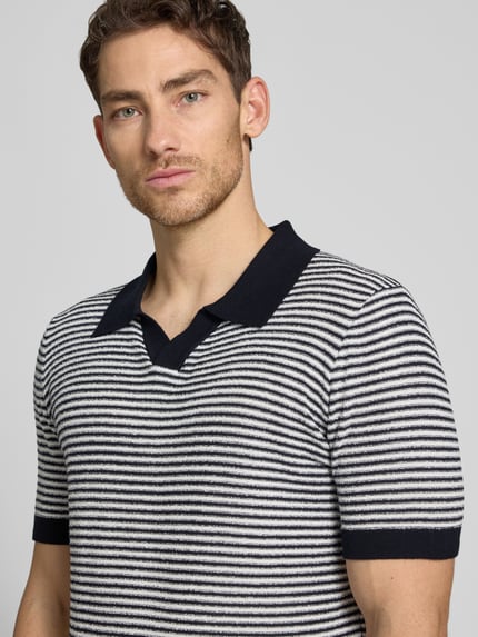 Męski model nosi Regular Fit Poloshirt mit V-Ausschnitt Modell 'RIANO' von CINQUE z mieszanki bawełny, krój regular fit, długość tyłu w rozmiarze M: 70 cm, paski, kolory czarny i biały, teksturowana powierzchnia, zbliżenie na górną część ciała