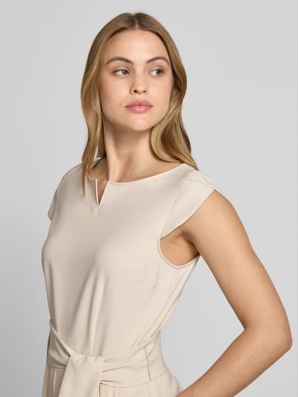 Frauenmodel trägt Regular Fit Jumpsuit mit Bügelfalten von Betty Barclay aus Elastischer-Material-Mix in Beige, Nahaufnahme Oberkörper. Rückenlänge bei Größe 36: 133 cm, Brustweite: 47 cm, Gesamtlänge: 40 cm, Innenbeinlänge: 62 cm, abnehmbares Stoffband, kurzärmelig.