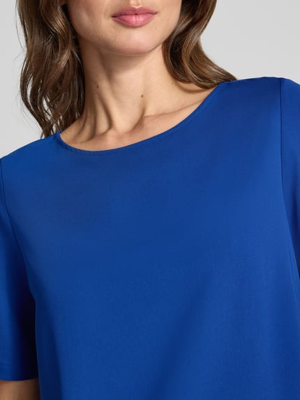 Vrouwenmodel draagt Regular fit blouse met korte mouwen met boothals van s.Oliver BLACK LABEL, effen blauw, gladde textuur, detailopname bovenlichaam. Dames Kurzarmbluse von s.Oliver BLACK LABEL.