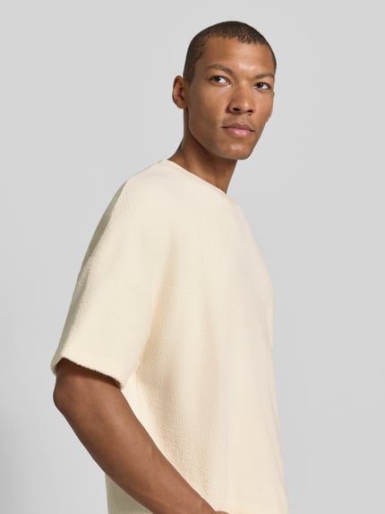 Männermodel trägt T-Shirt mit Frottee-Struktur von AMERICAN VINTAGE in Creme mit Struktur, Rundhals und kurzen Ärmeln, Nahaufnahme Oberkörper.